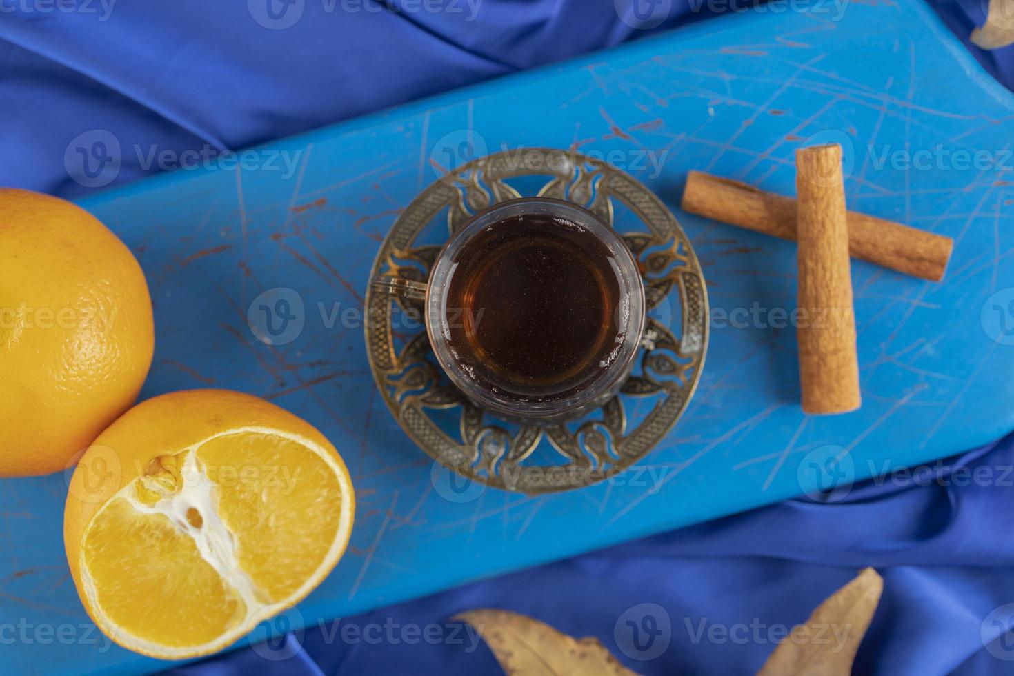 bicchiere di tè, arancia e bastoncini di cannella su un bordo blu foto