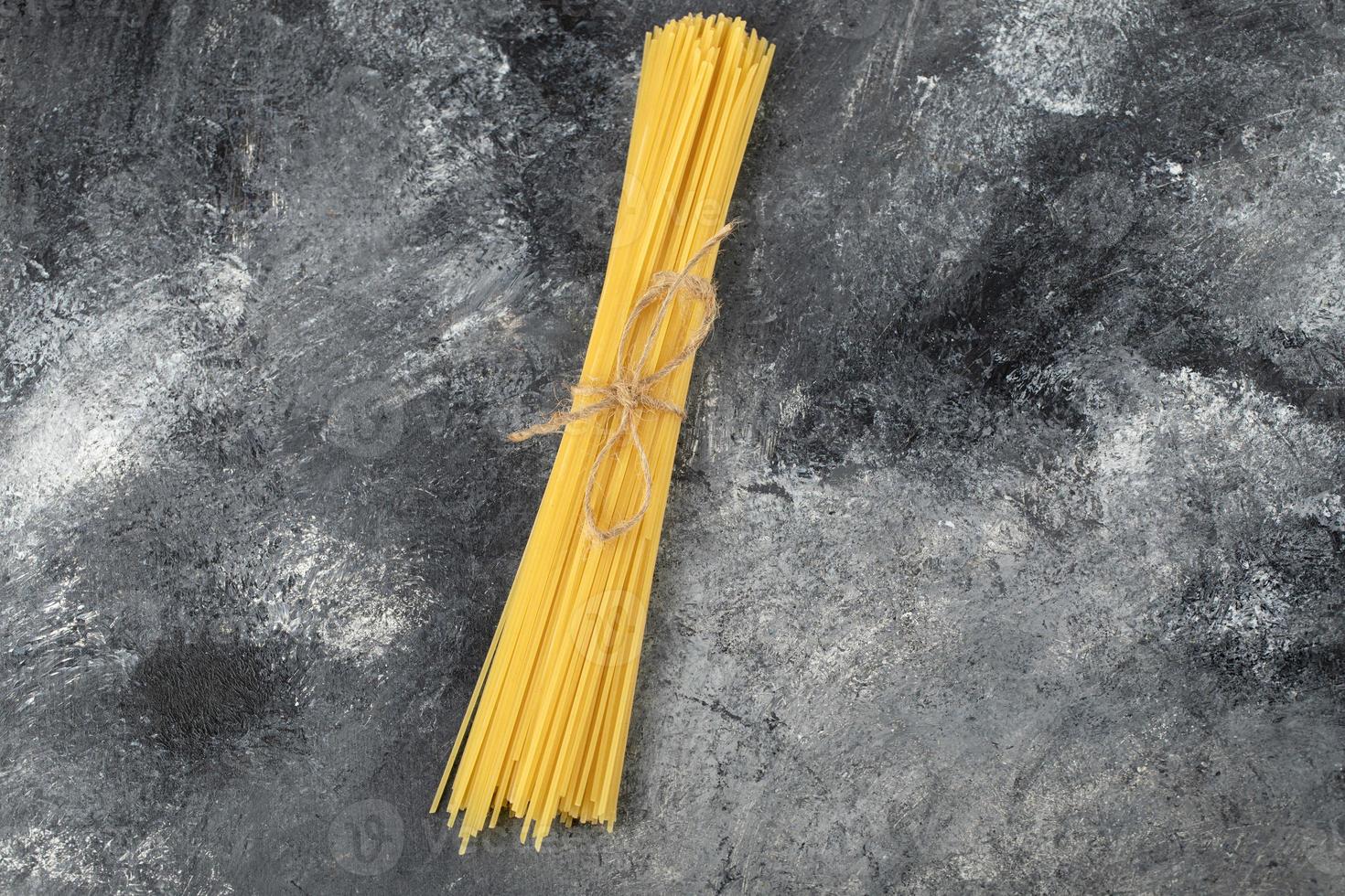 spaghetti secchi legati con una corda su uno sfondo di marmo foto