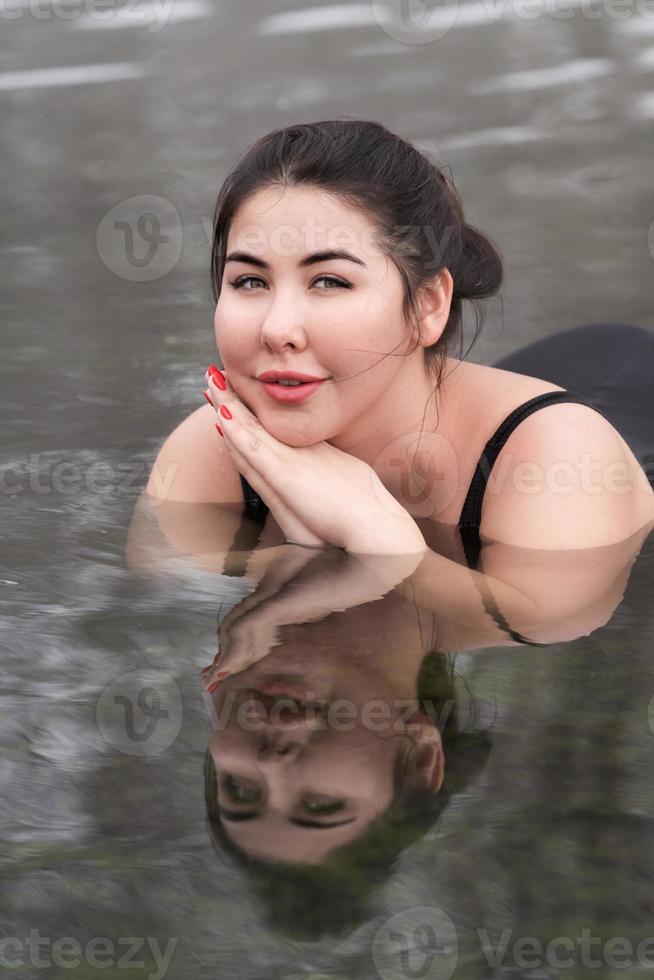 esteso dimensioni giovane donna nel nero nuoto costume dire bugie nel minerale acqua nel all'aperto piscina a terme foto