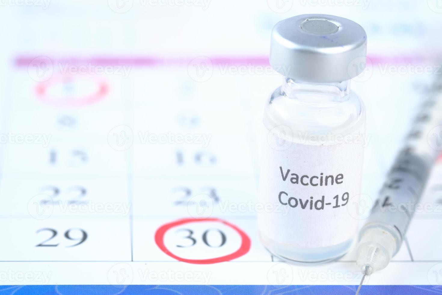 primo piano del vaccino contro il coronavirus e la siringa su un calendario con un cerchio rosso foto