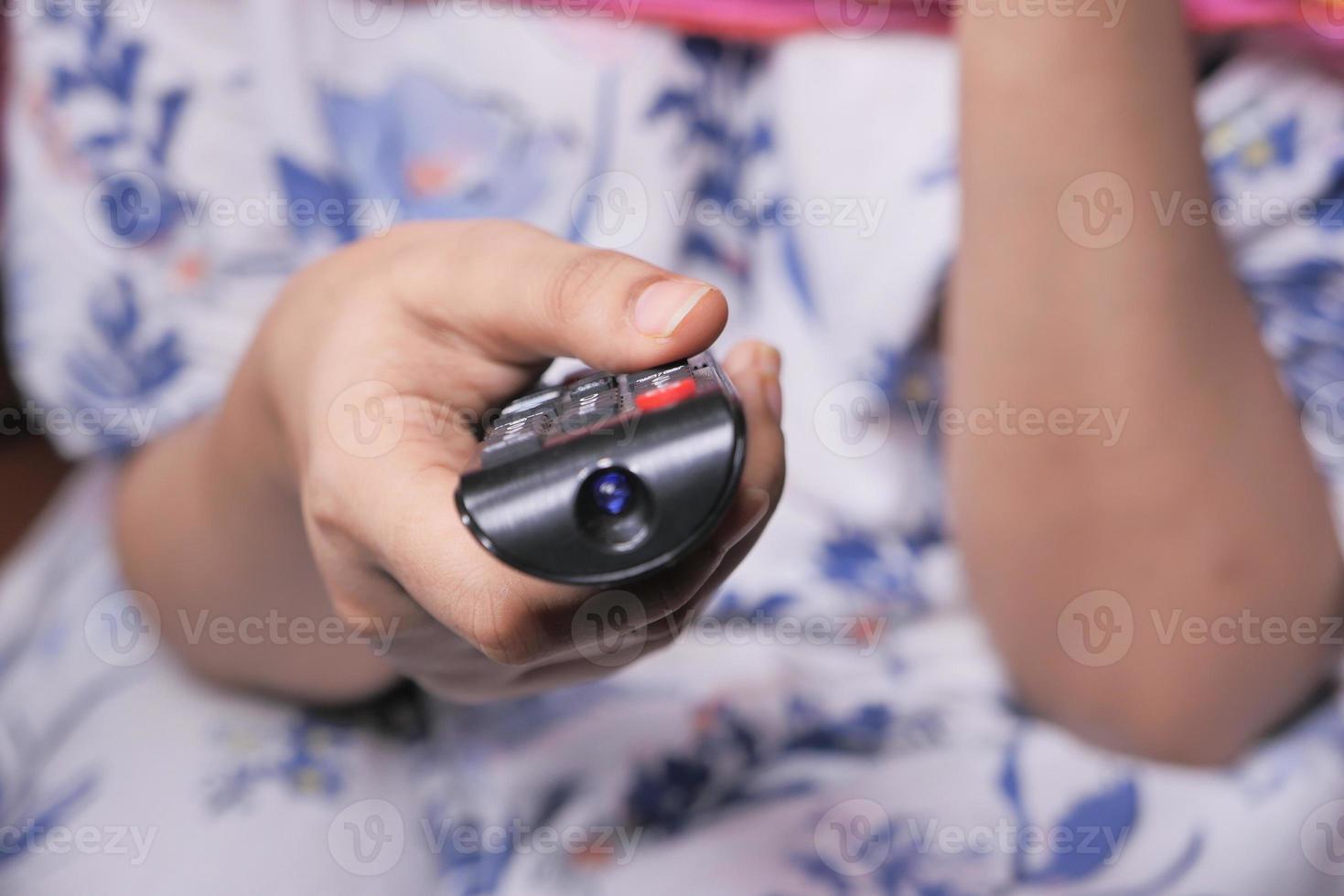 mano della donna che tiene il telecomando della tv foto