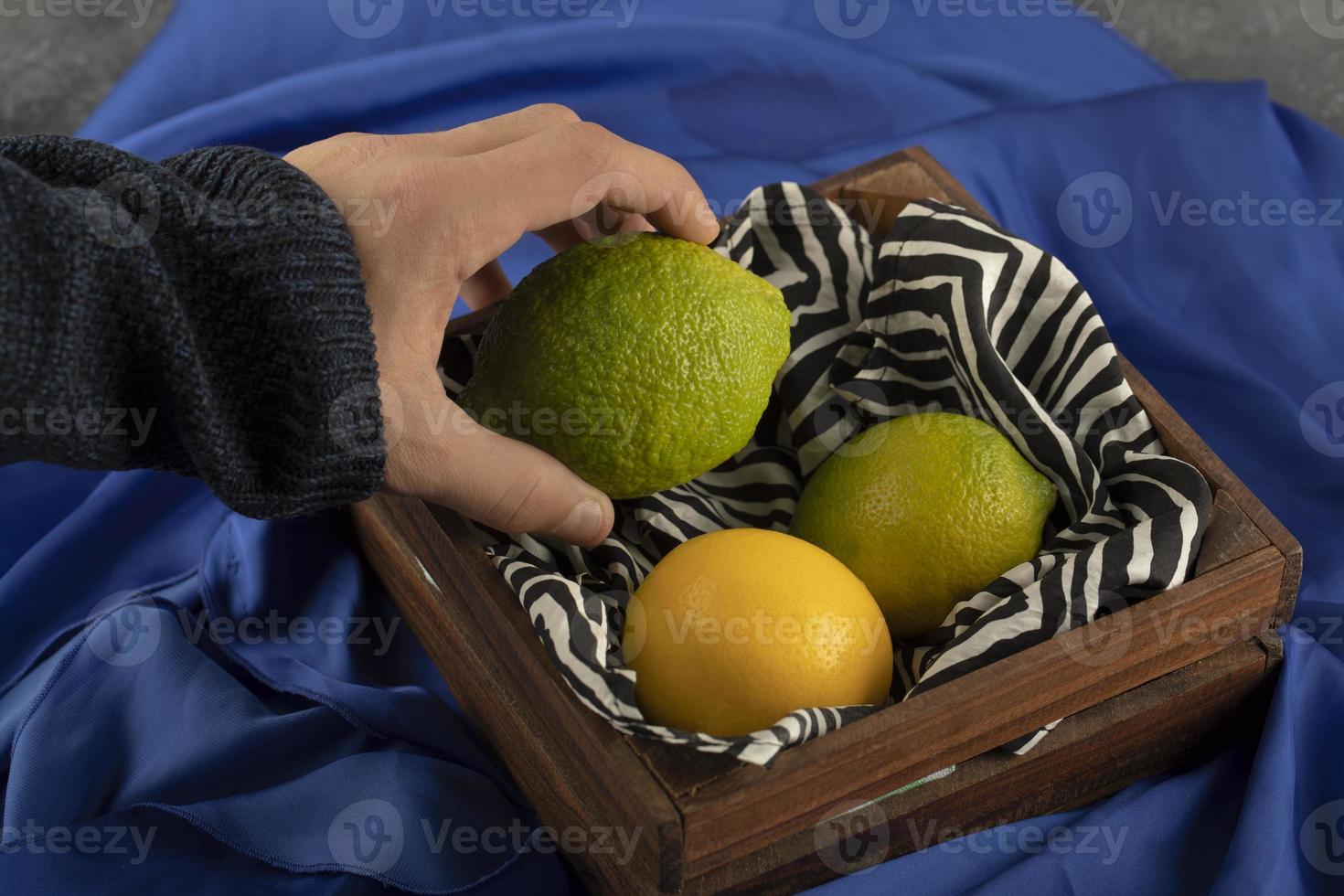 mano d'uomo prendendo un lime da un cesto di legno foto