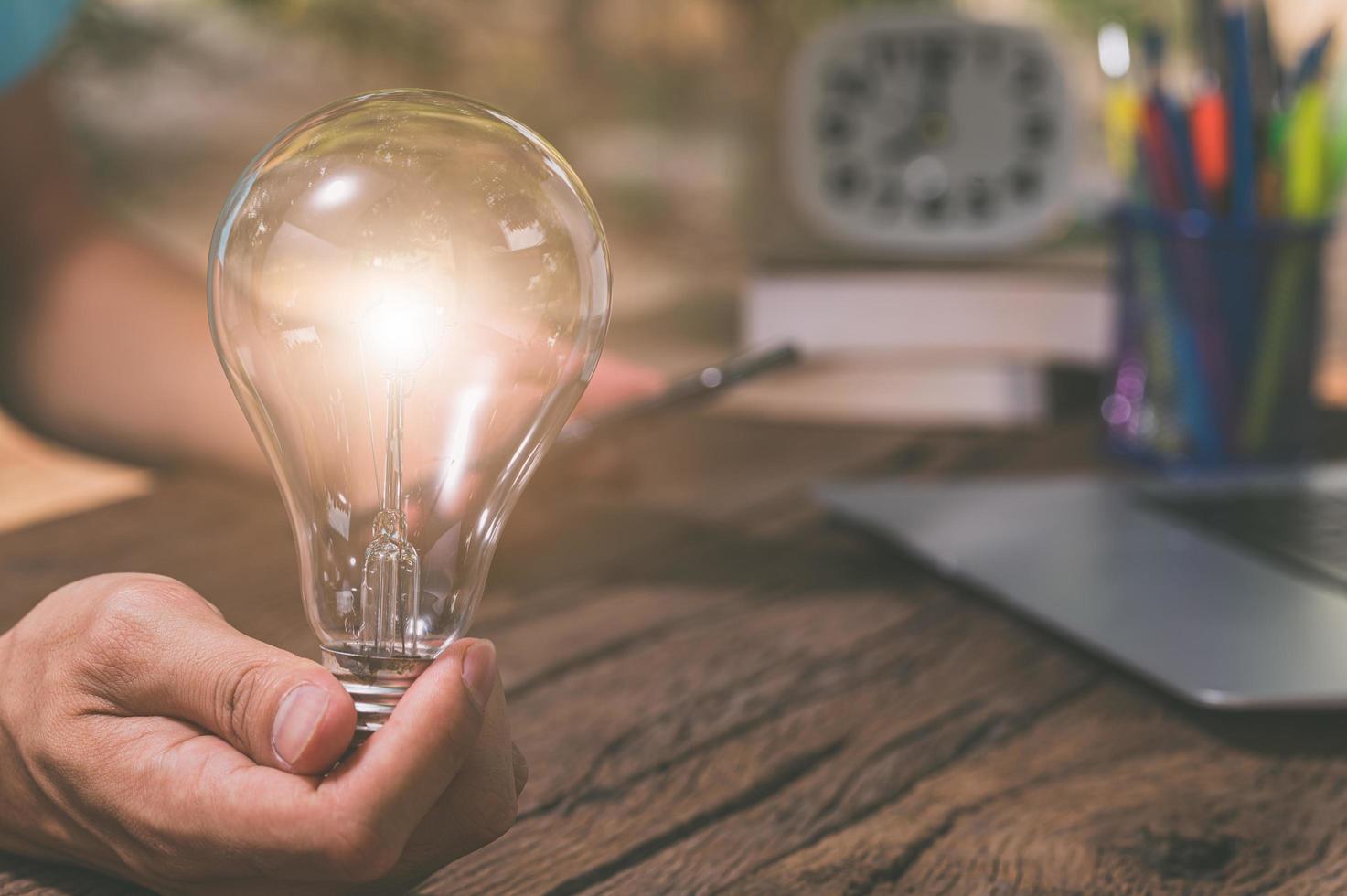 una persona in possesso di una lampadina accanto a un computer portatile, un nuovo concetto di idee foto