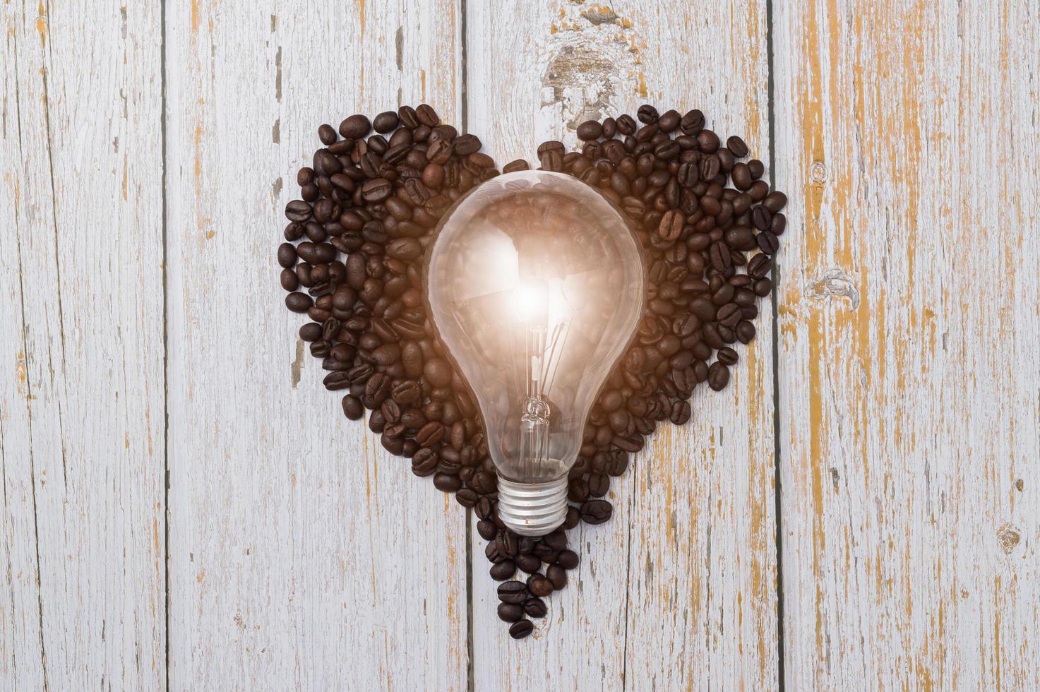 chicchi di caffè a forma di cuore e una lampadina su un tavolo di legno foto