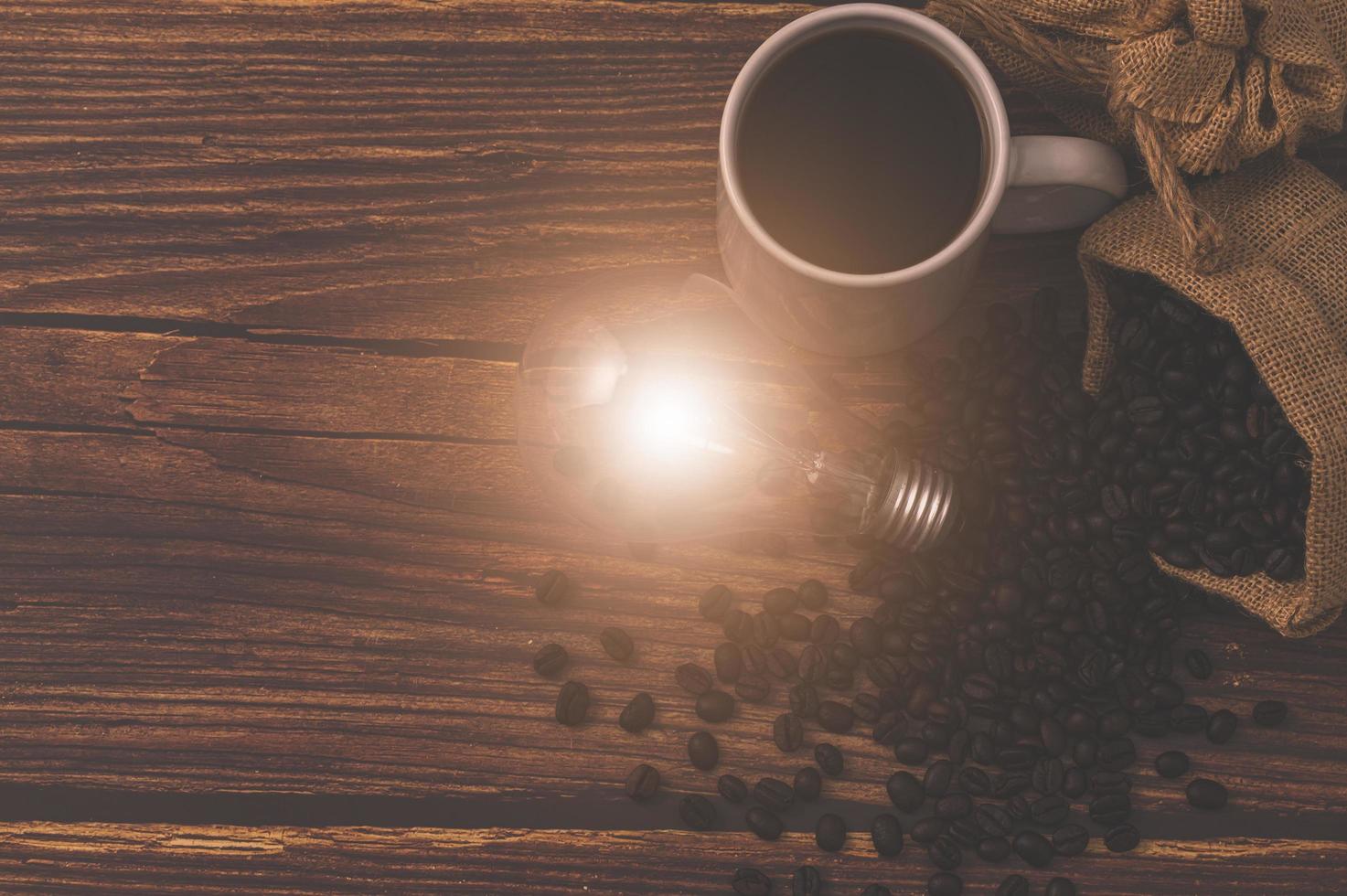 tazza di caffè e una lampadina che emette energia su un tavolo di legno foto