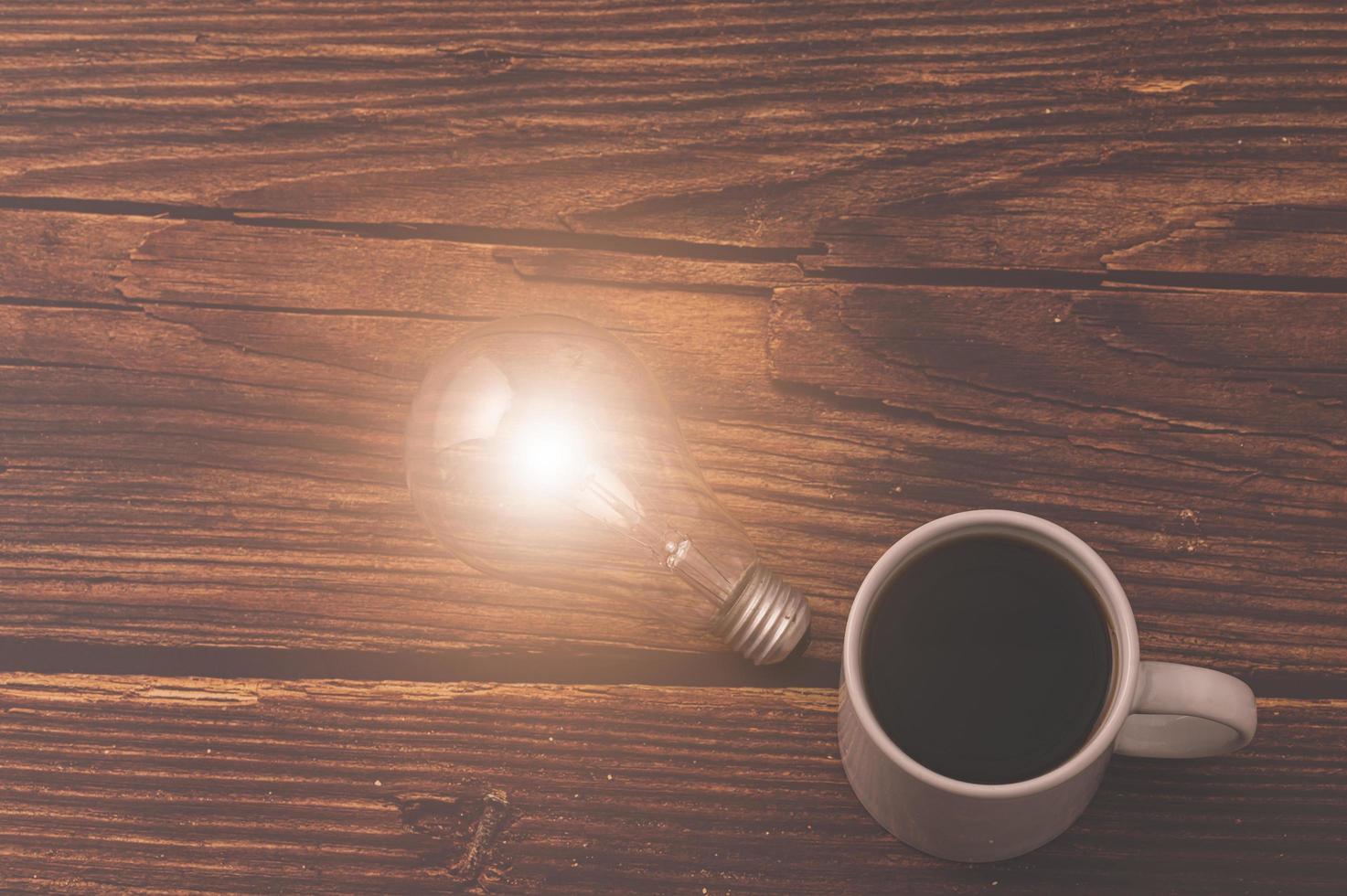 tazza di caffè e una lampadina che emette energia su un tavolo di legno foto