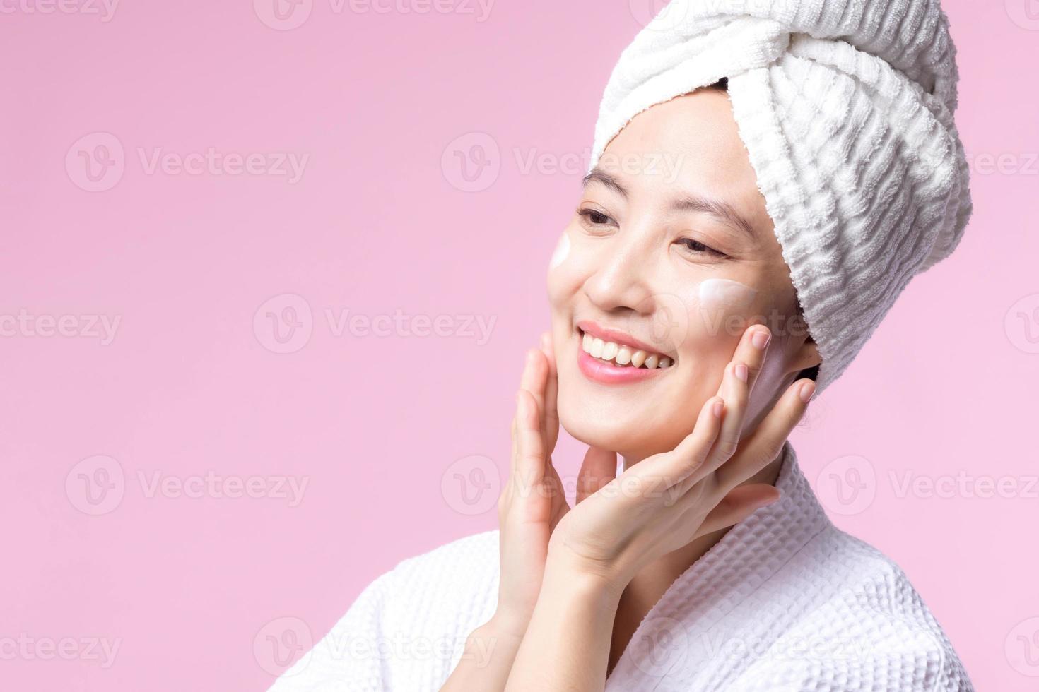 giovane asiatico donna l'applicazione facciale cura della pelle viso crema, cosmetico idratante su salutare naturale pelle rendere su viso. ritratto raggiante Sorridi ragazza persona modello con cura bellezza Prodotto, terme, cosmetologia. foto