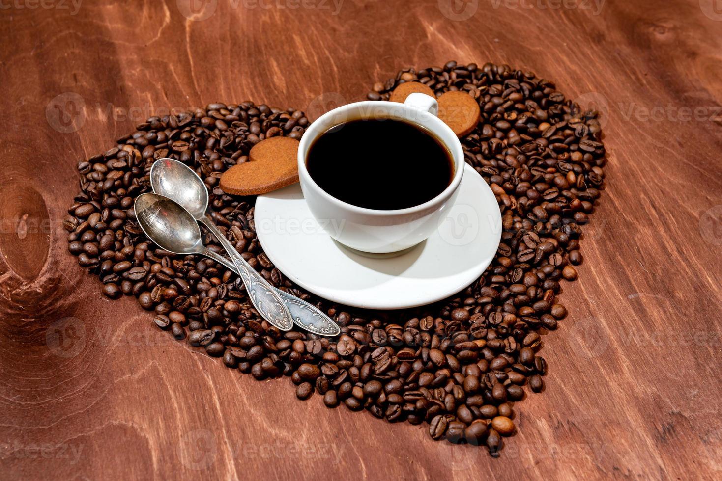 tazza di caffè bianco, pan di zenzero a forma di cuore e due cucchiai su un cuore foto