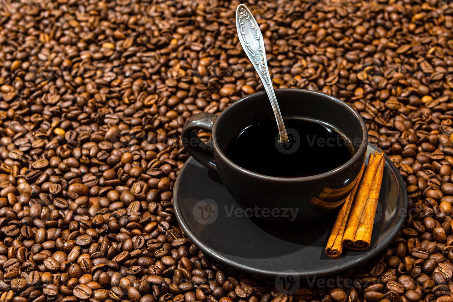 tazza di caffè nero e bastoncini di cannella sullo sfondo di chicchi di caffè foto