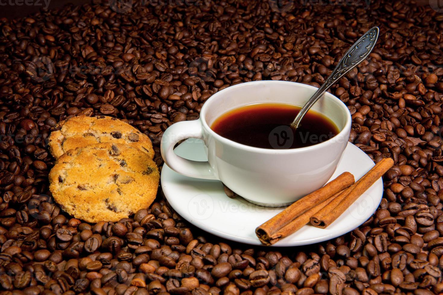 tazza di caffè bianco, bastoncini di cannella e biscotti sullo sfondo di chicchi di caffè foto