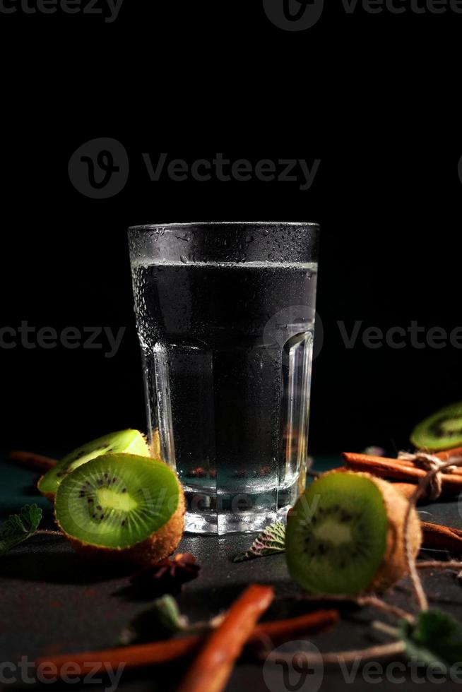 un' bicchiere di freddo acqua su un' verde sfondo. decorato con fetta kiwi, cannella bastoni, badiano, menta le foglie. copia spazio foto