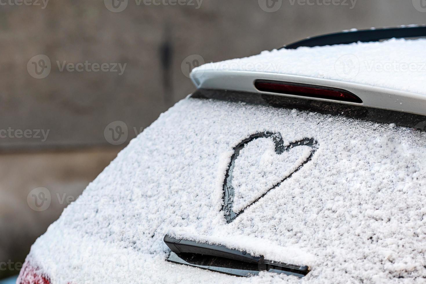 a forma di cuore sul lunotto della macchina coperta di neve foto