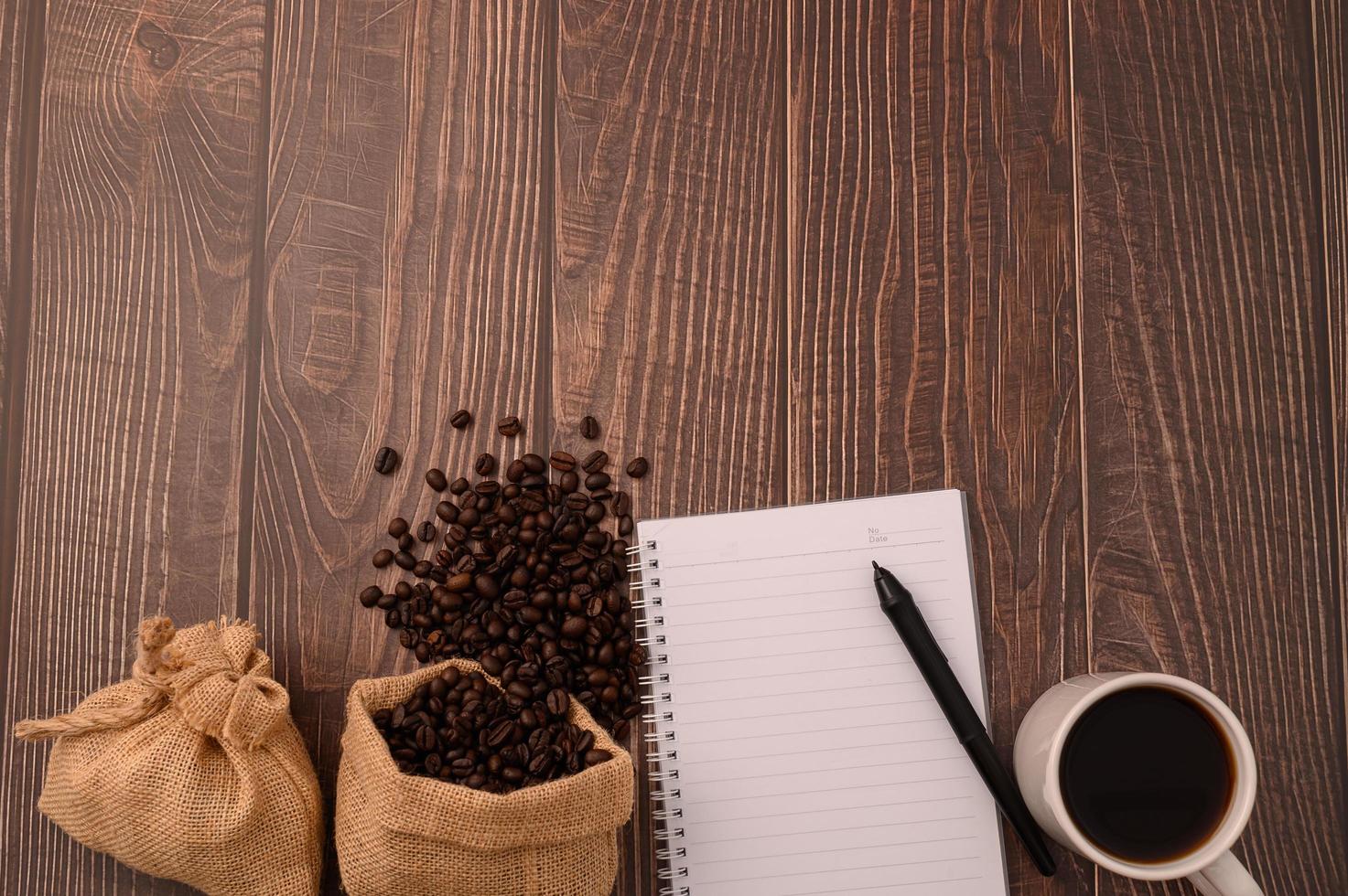 caffè, chicchi di caffè e un taccuino con una penna su una scrivania in legno foto