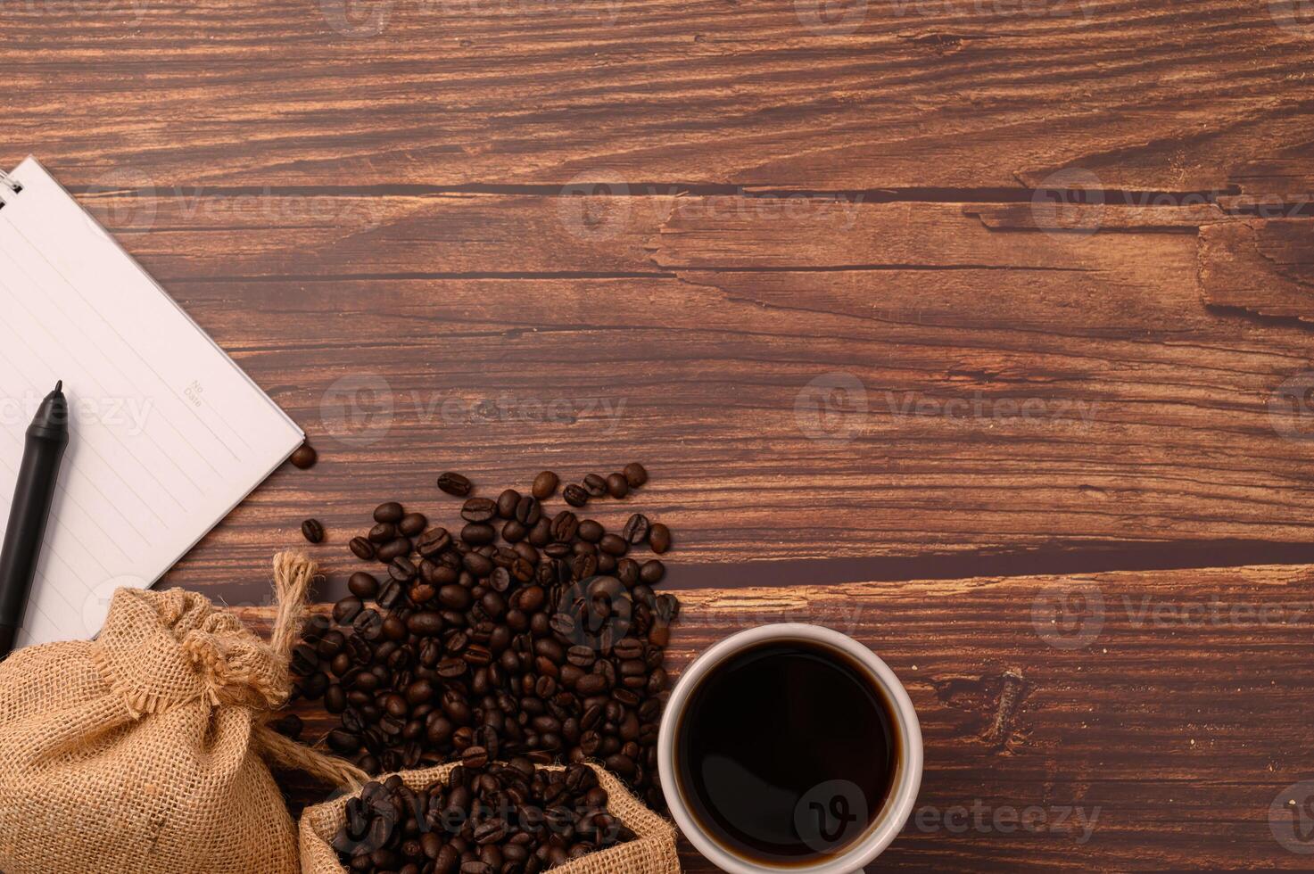 caffè, chicchi di caffè e un taccuino con una penna su una scrivania in legno foto