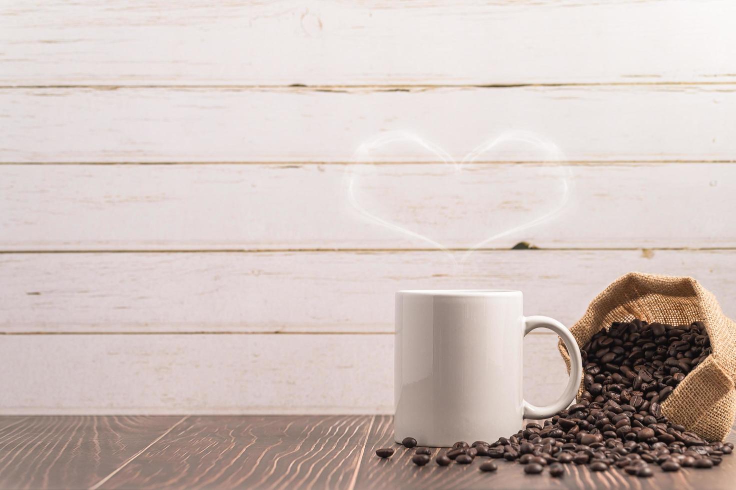 una tazza di caffè che fa vapore a forma di cuore con un sacchetto di chicchi di caffè su un tavolo di legno foto