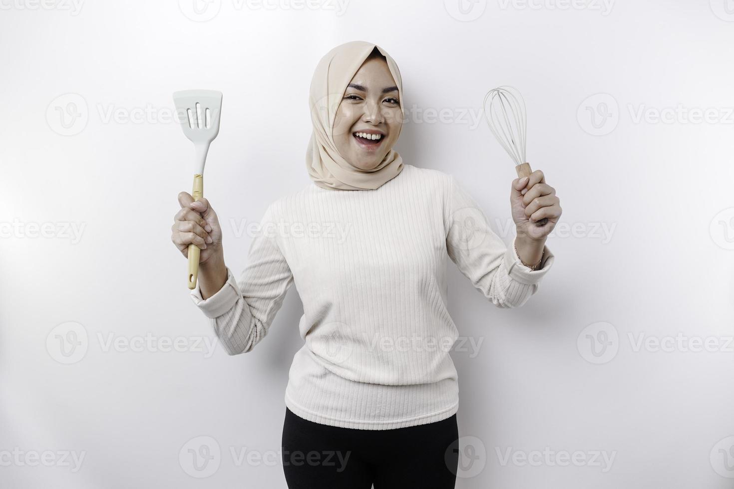 eccitato asiatico musulmano donna indossare un' foulard, Tenere cucinando merce e sorridente, isolato di bianca sfondo foto