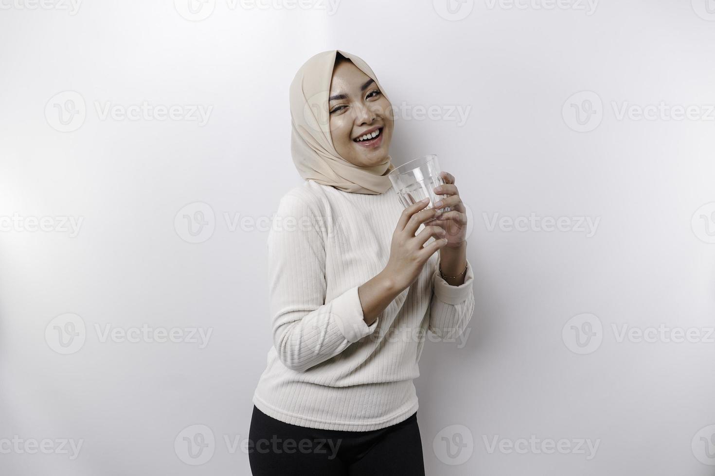 gioioso asiatico musulmano donna indossare foulard è potabile un' bicchiere di acqua, isolato su bianca sfondo. foto