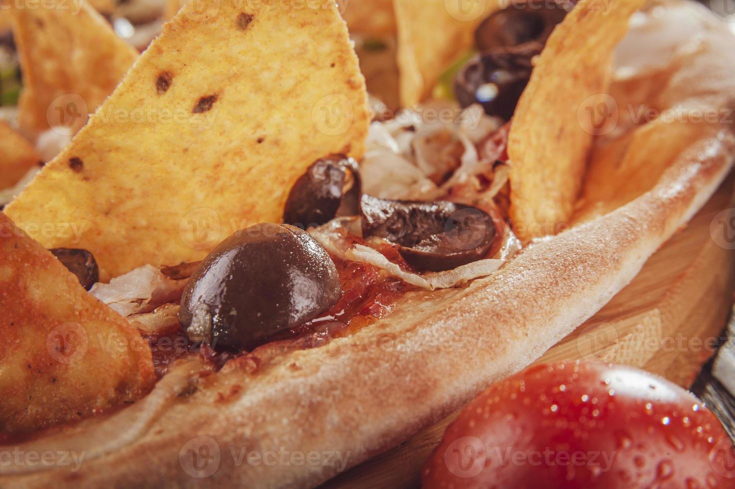 pizza con mozzarella, cipolla, peperoni, olive nere, peperoni verdi, nachos e origano foto