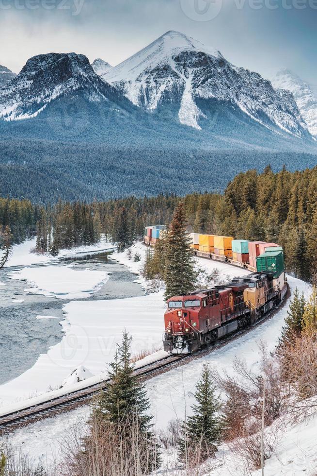 moranti curva con iconico rosso carico treno passaggio attraverso arco valle e roccioso montagne nel inverno a Banff nazionale parco foto