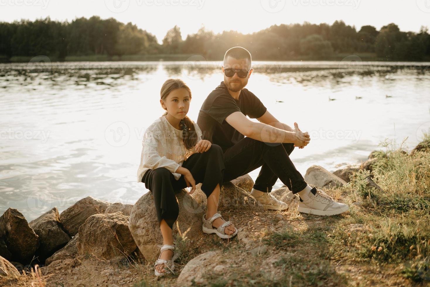 un giovane padre con la barba e gli occhiali da sole posa con la sua graziosa figlia sulla costa foto