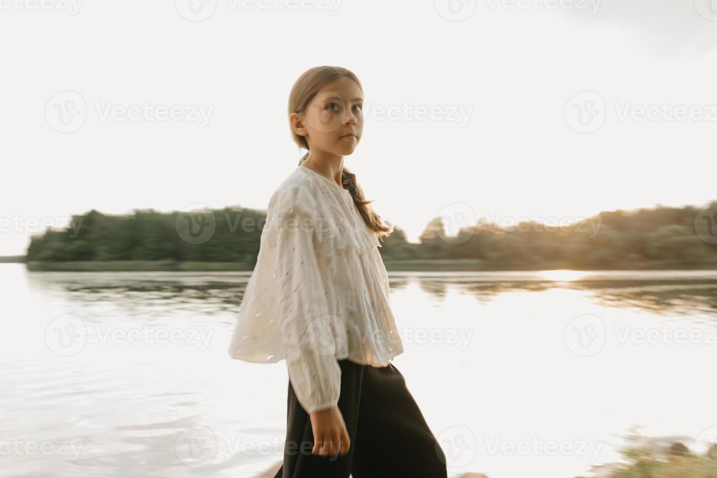 un ritratto sfocato di una giovane ragazza che sta camminando sulla costa del lago al tramonto foto
