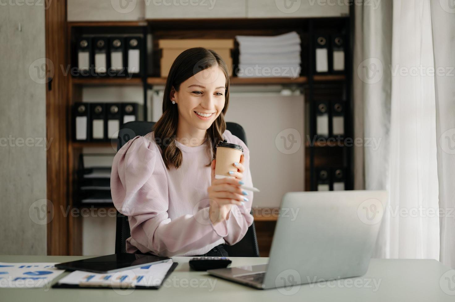 giovane attraente asiatico donna sorridente pensiero pianificazione scrittura nel taccuino, tavoletta e il computer portatile Lavorando a partire dal casa, guardare a telecamera a ufficio foto