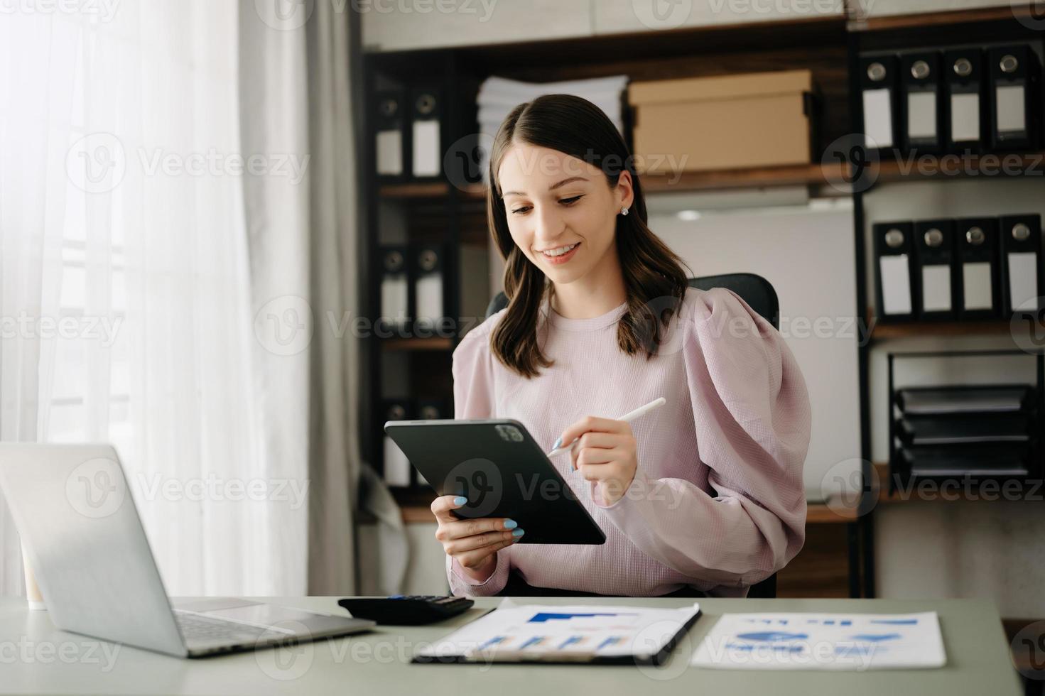 fiducioso attività commerciale esperto attraente sorridente giovane donna digitando il computer portatile ang Tenere digitale tavoletta su scrivania nel ufficio. foto