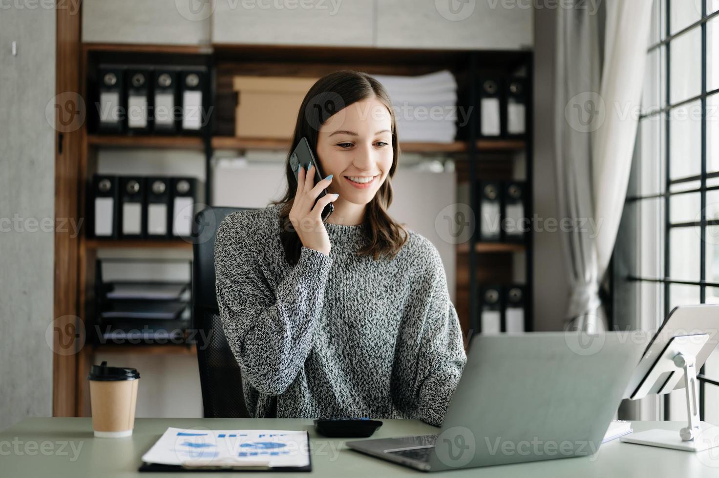 giovane bellissimo donna digitando su tavoletta e il computer portatile mentre seduta a il Lavorando di legno tavolo ufficio foto