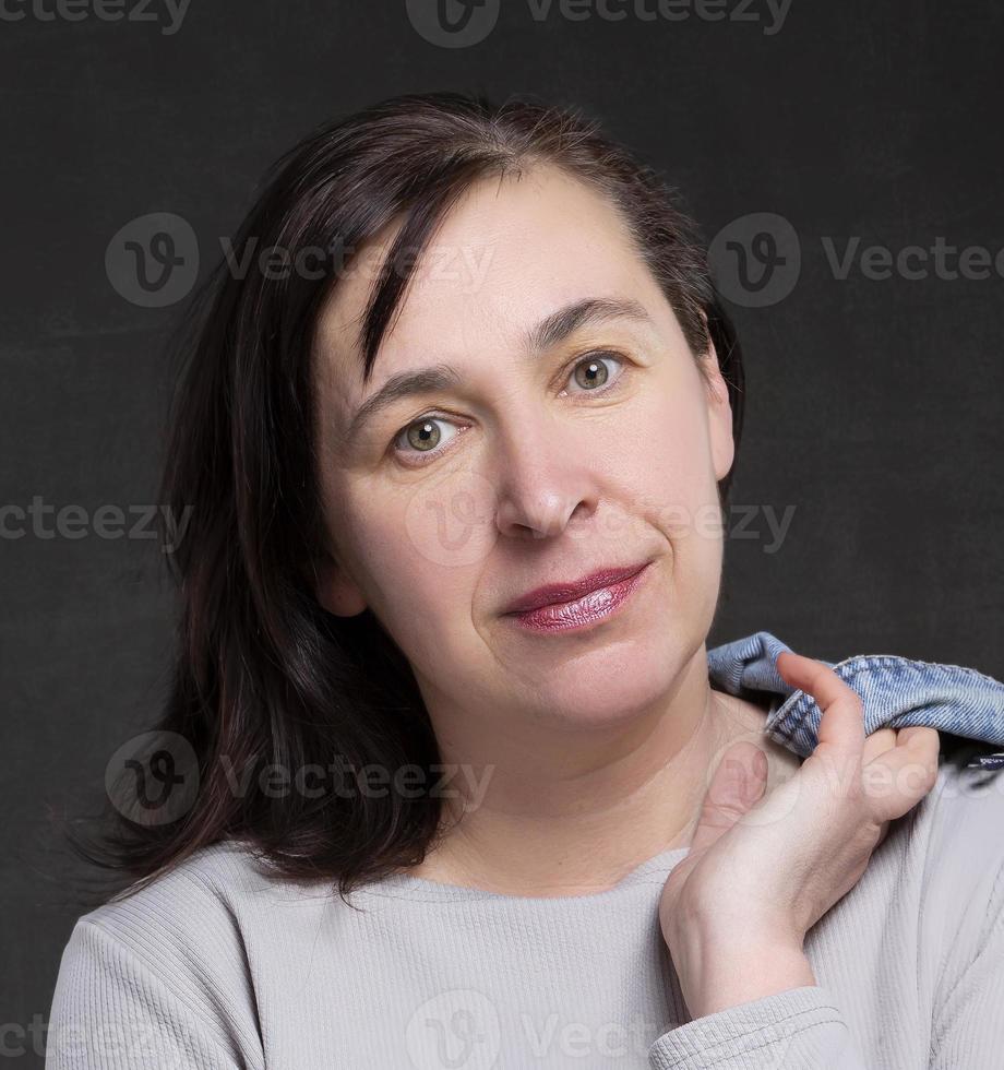 bellissimo cinquanta anno vecchio donna con buio capelli su un' grigio sfondo. ritratto di un' di mezza età donna. foto