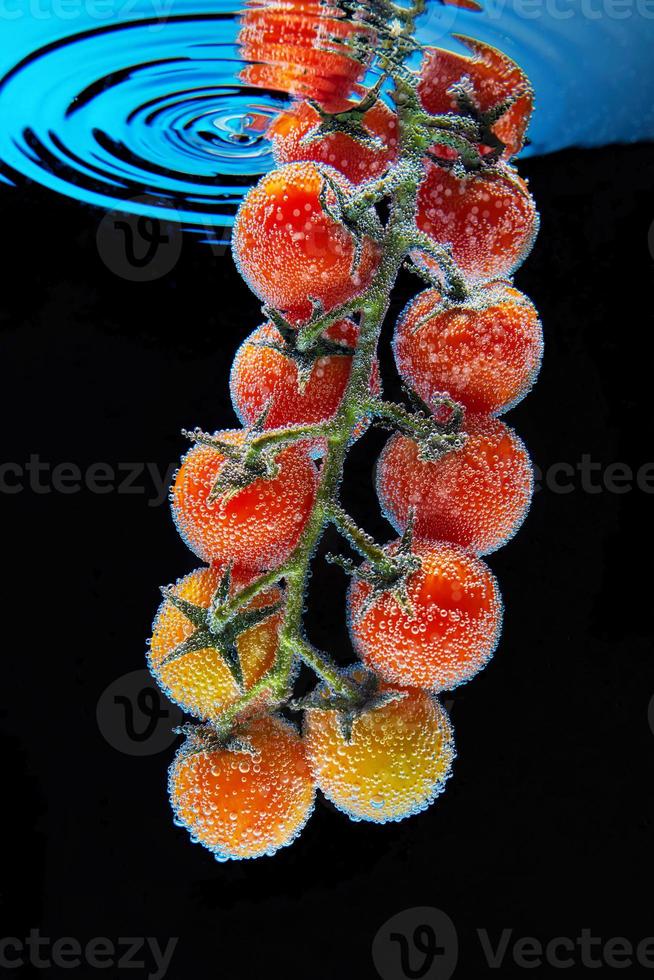 un ramo di pomodorini rossi con foglie verdi ricoperto di bolle di gas di acqua minerale foto
