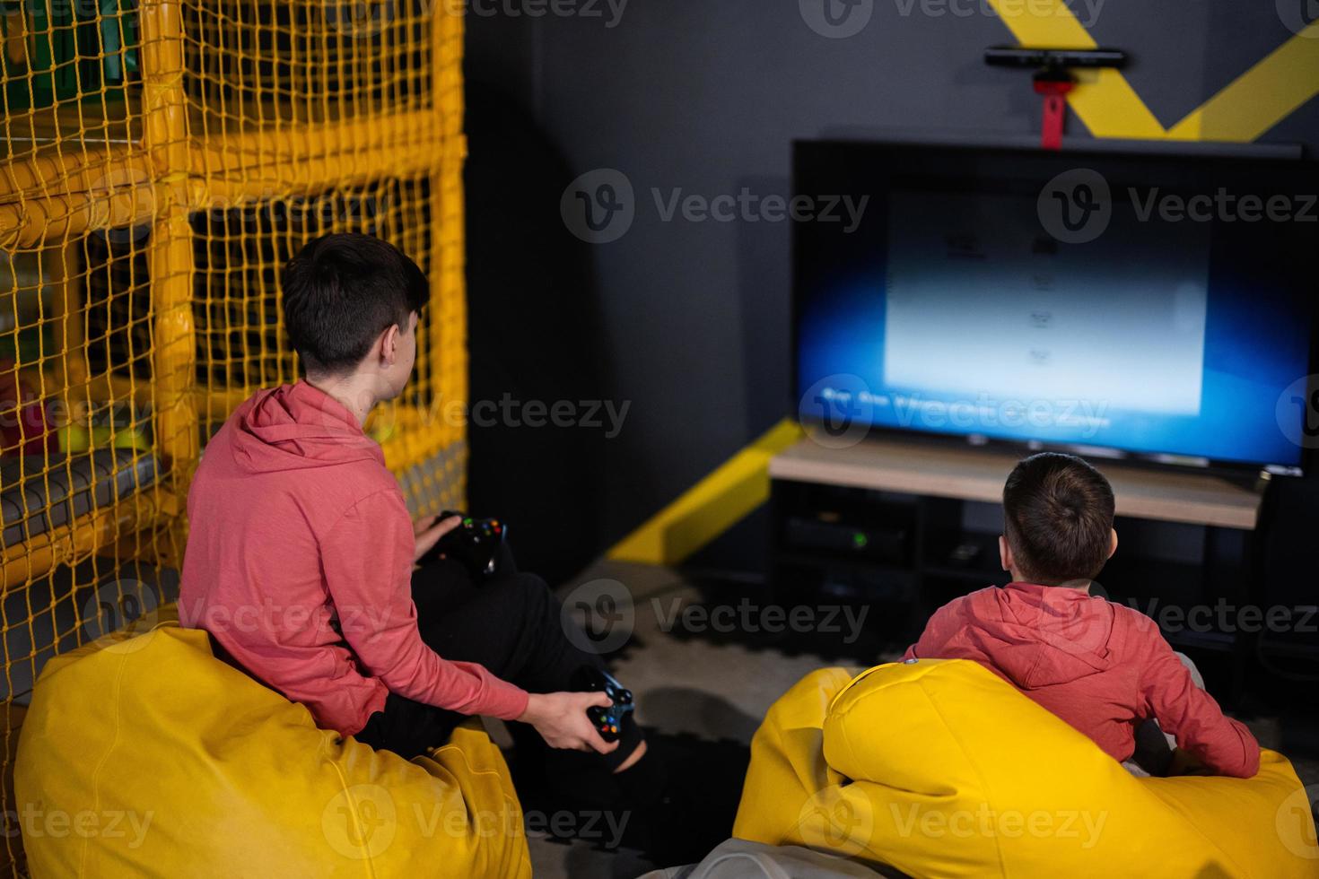 Due fratelli giocando video gioco console, seduta su giallo pouf nel bambini giocare centro. foto