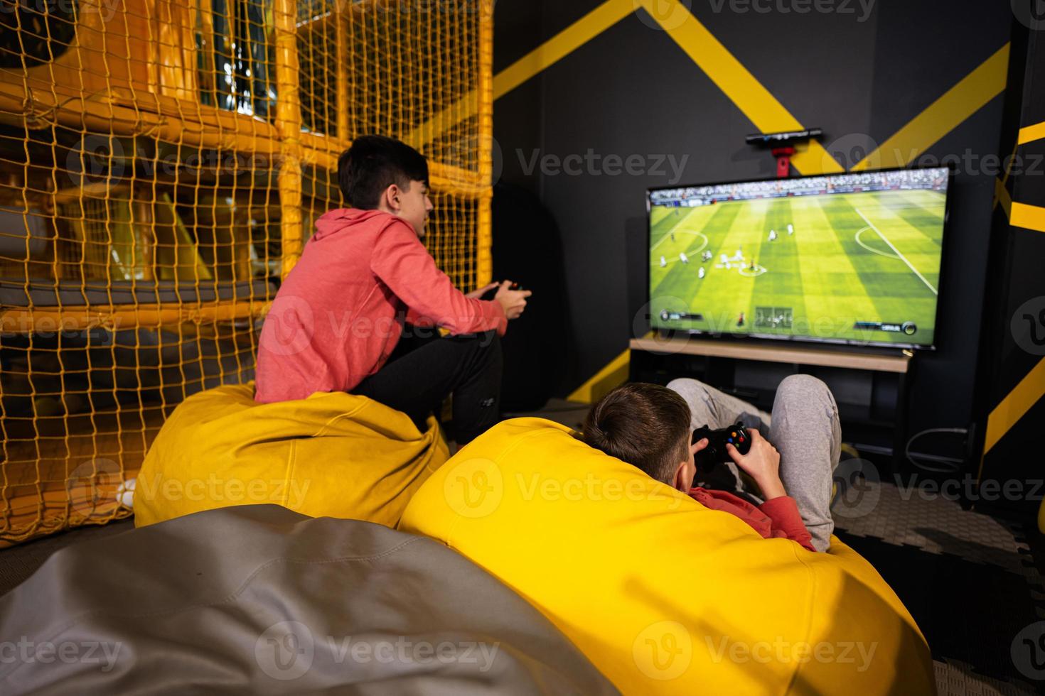 Due fratelli giocando calcio video gioco console, seduta su giallo pouf nel bambini giocare centro. foto