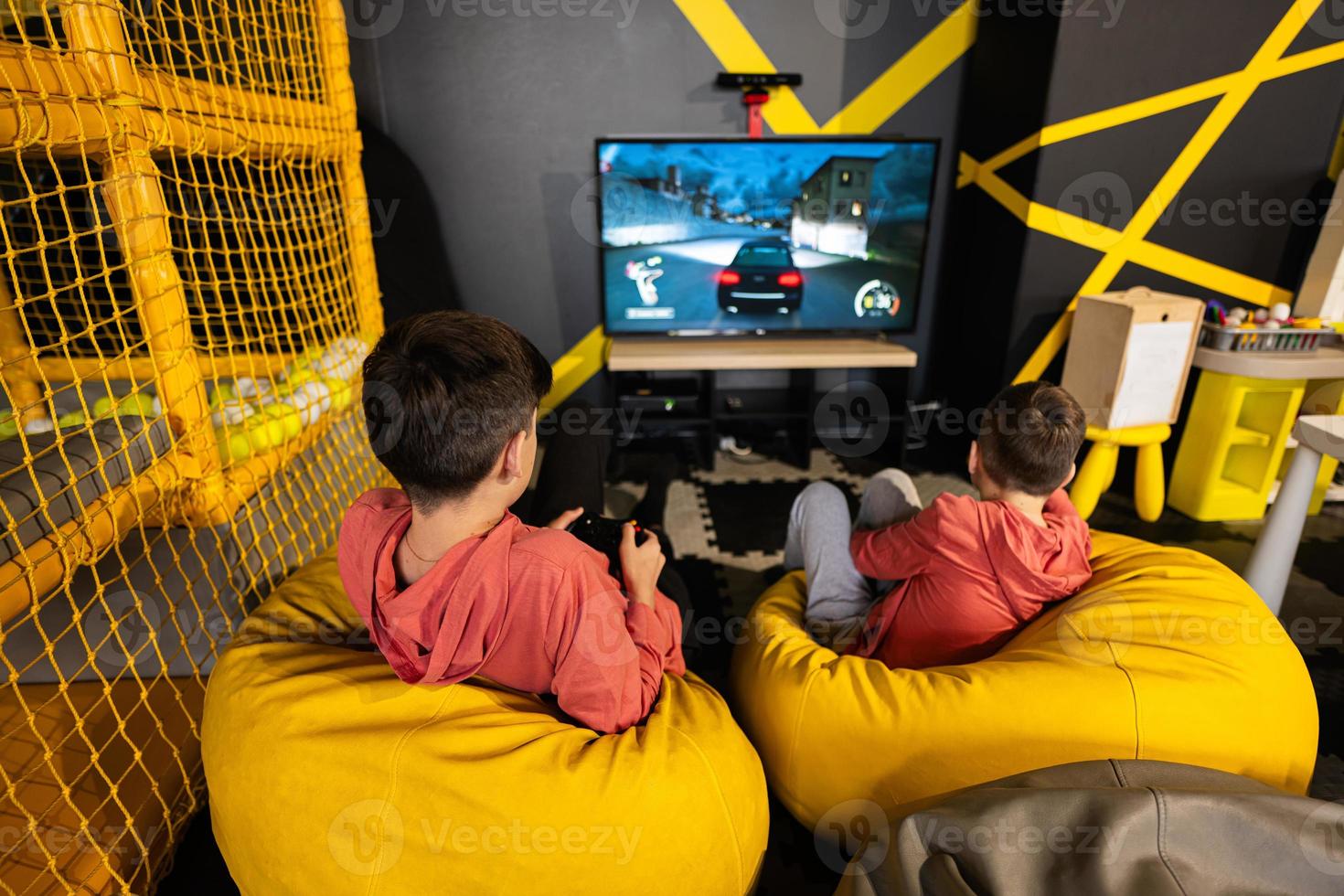 Due fratelli giocando gara video gioco console, seduta su giallo pouf nel bambini giocare centro. foto