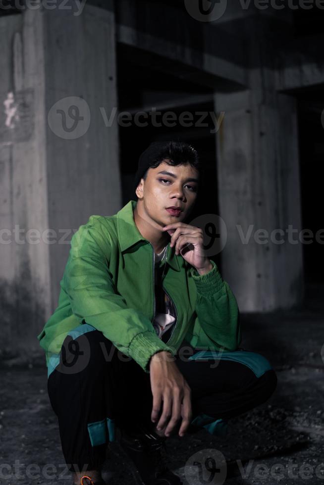 un asiatico uomo squat mentre indossare un' verde giacca foto