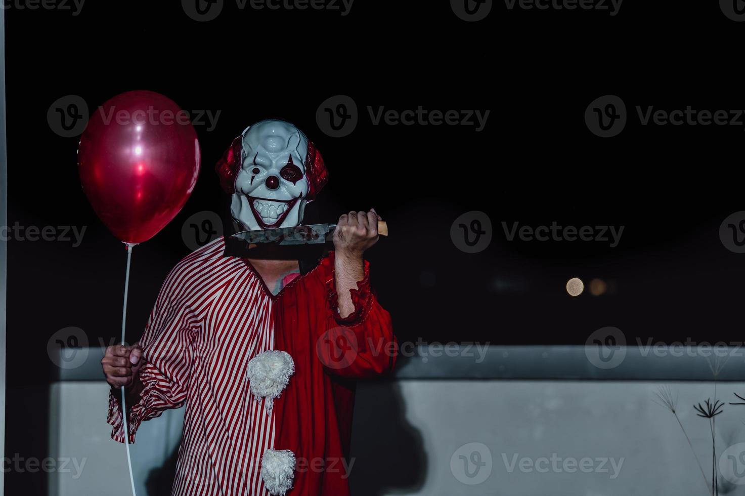 asiatico bello uomo indossare clown maschera con arma a il notte scena, halloween Festival concetto, orrore pauroso foto di un' uccisore nel arancia stoffa, male clown charactor