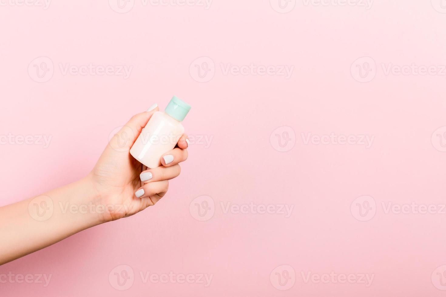 femmina mano Tenere crema bottiglia di lozione isolato. ragazza dare tubo cosmetico prodotti su rosa sfondo foto