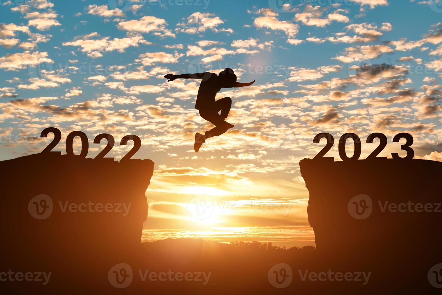 contento nuovo anno 2023 concetto. silhouette di uomo saltare su il scogliera fra 2022 per 2023 anni al di sopra di tramonto o Alba sfondo. foto