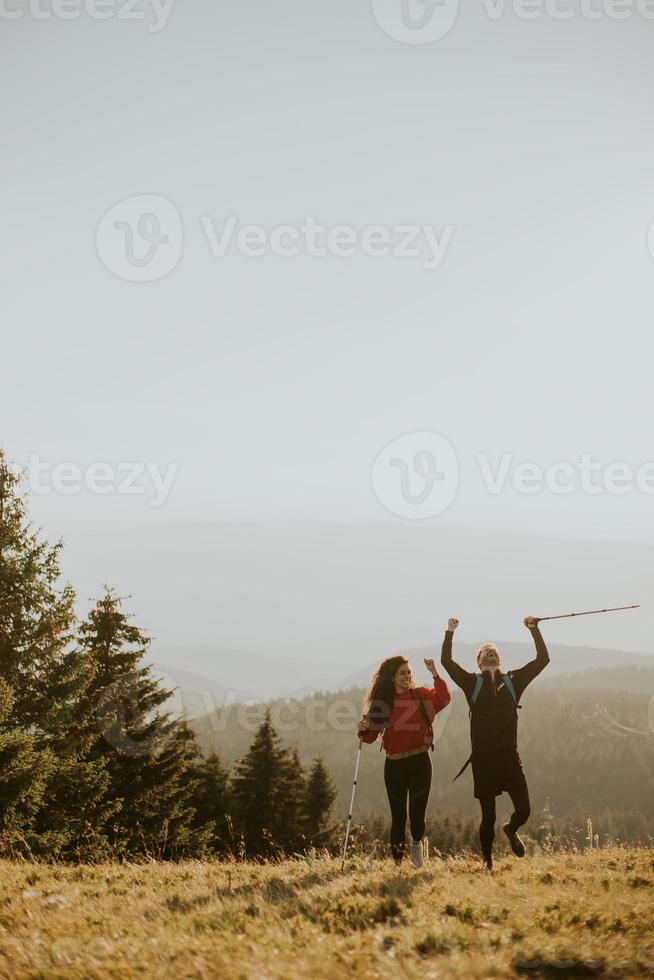 coppia sorridente che cammina con zaini su verdi colline foto