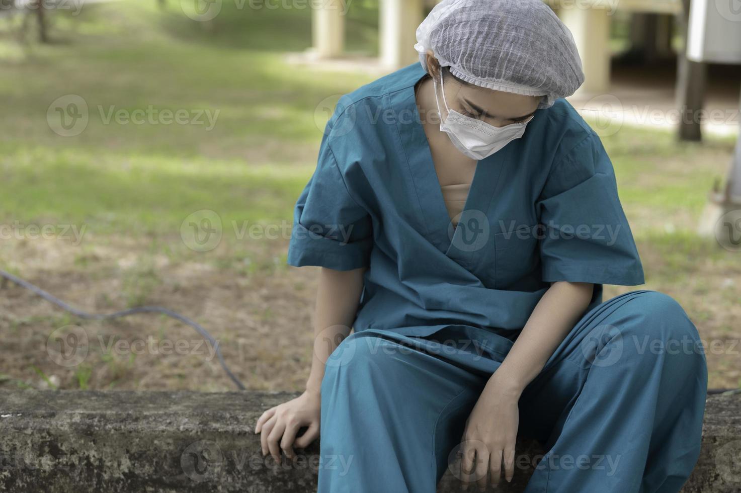 stanco depresso donna asiatica scrub infermiera indossa maschera facciale uniforme blu siede sul pavimento dell'ospedale, giovane donna medico stressato dal duro lavoro foto