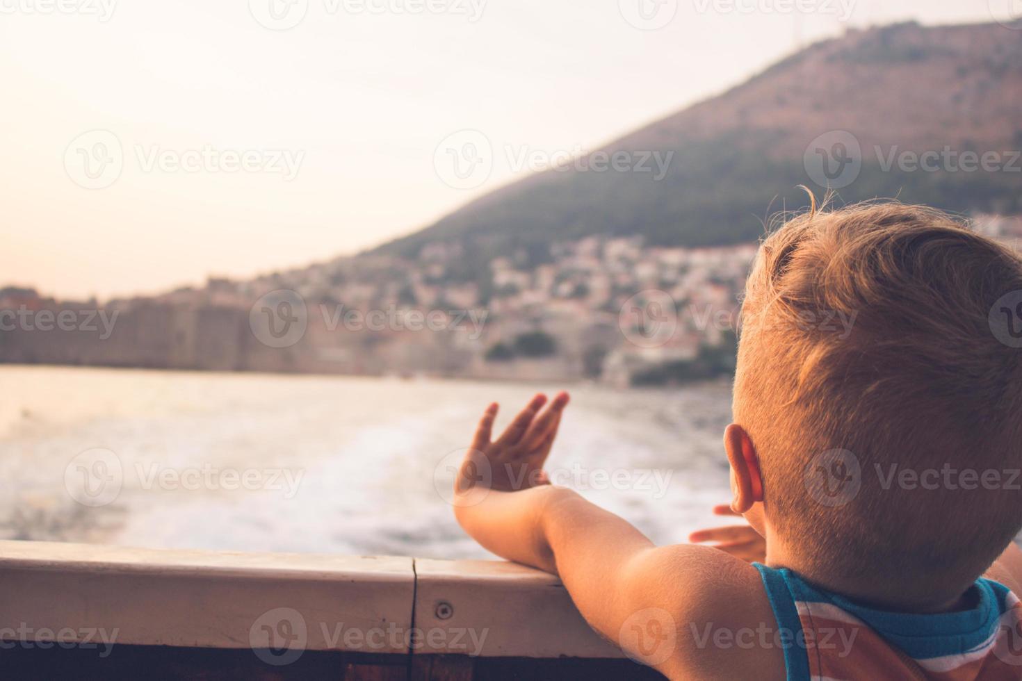 ragazzino che viaggia in barca a vela e salutando al tramonto foto