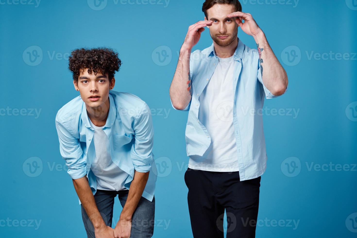 dai capelli ricci tipo nel un' blu camicia Appoggiato inoltrare e un' biondo uomo su un' blu sfondo amici foto