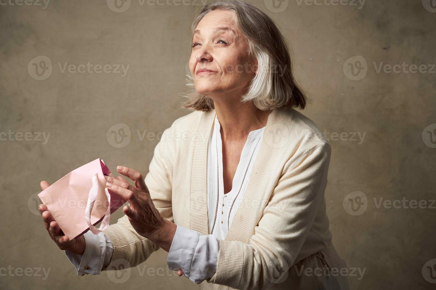 anziano donna nel un' condimento toga con un' regalo nel sua mani compleanno cura foto