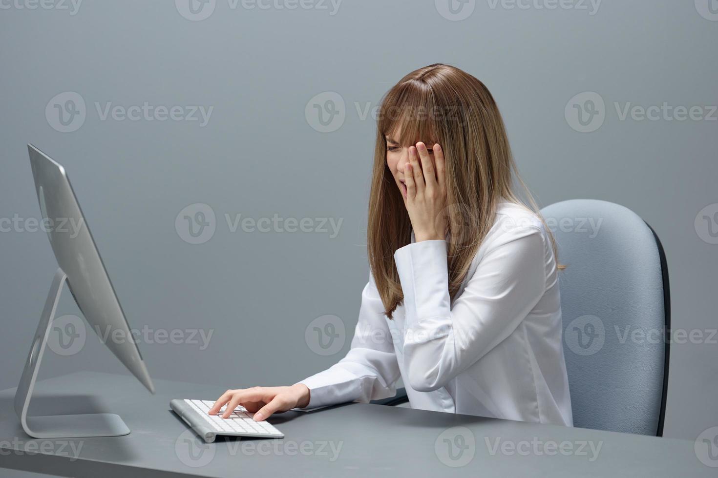 pianto bella bionda donna d'affari fatto critico sbaglio utilizzando del desktop computer fare facepalm seduta nel grigio moderno ufficio. a distanza lavoro, tecnologia e carriera professione concetto. copia spazio foto