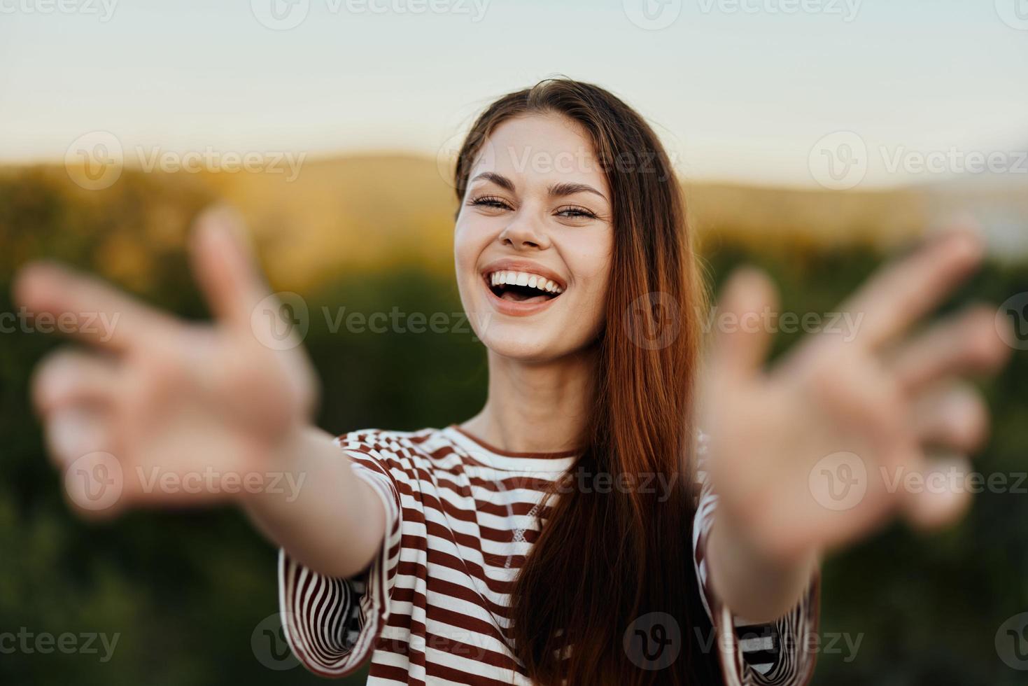 donna sorridente mentre guardare a il telecamera e traino sua mani per il telecamera avvicinamento nel natura con un' Visualizza di il montagne. contento viaggio stile di vita Seguire me foto