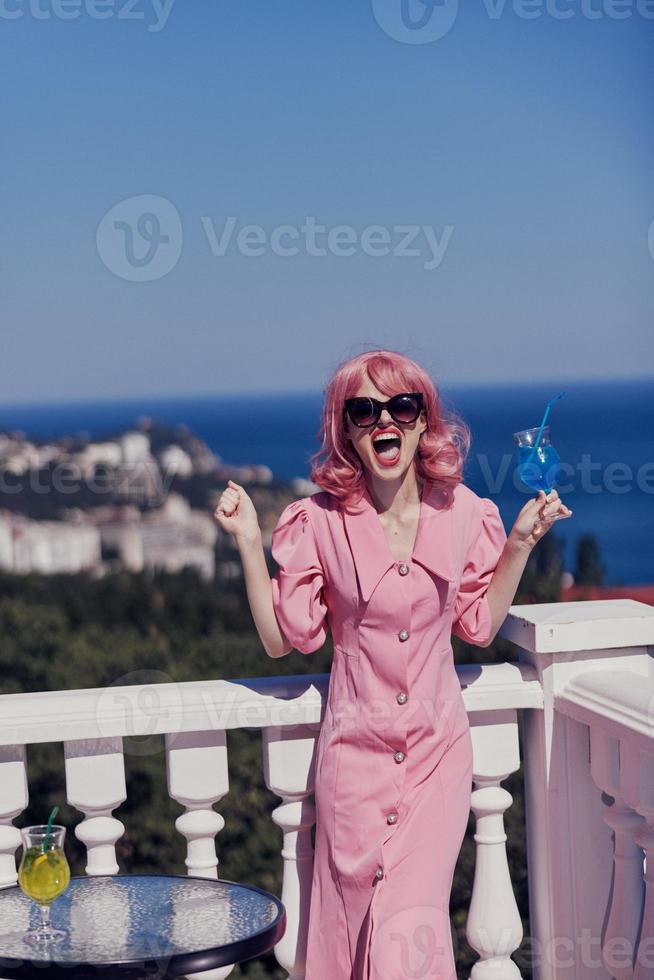 alla moda donna nel un' rosa vestito nel occhiali da sole con un' cocktail inalterato foto