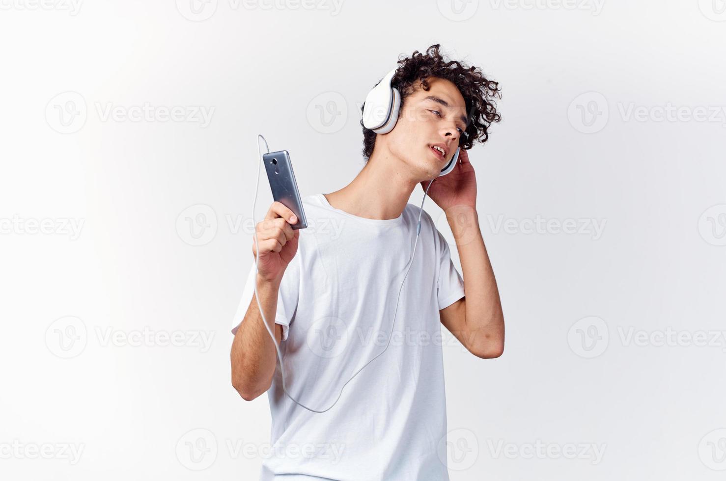 uomo con Riccio capelli nel bianca maglietta ascoltando per musica con cuffie Telefono tecnologia foto