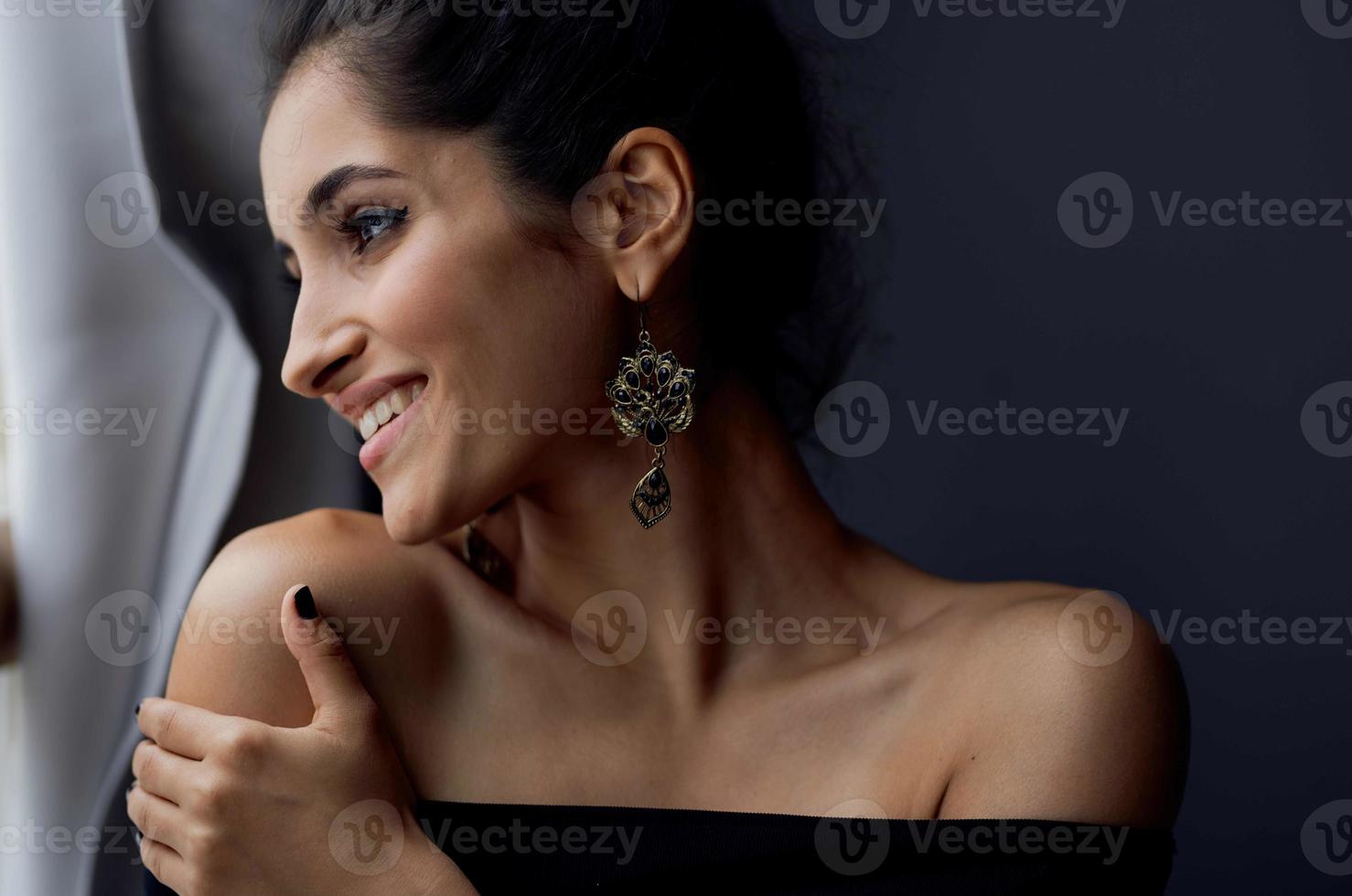 bellissimo donna vicino finestra in posa attraente Guarda orecchini elegante stile foto