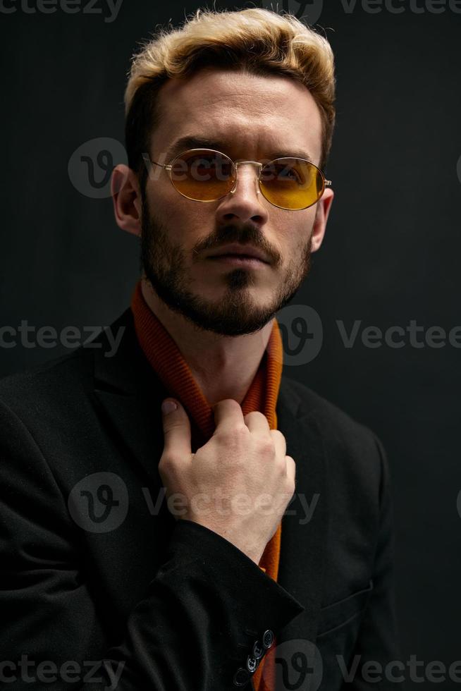 elegante uomo con bicchieri biondo nero giacca arancia maglione buio sfondo foto