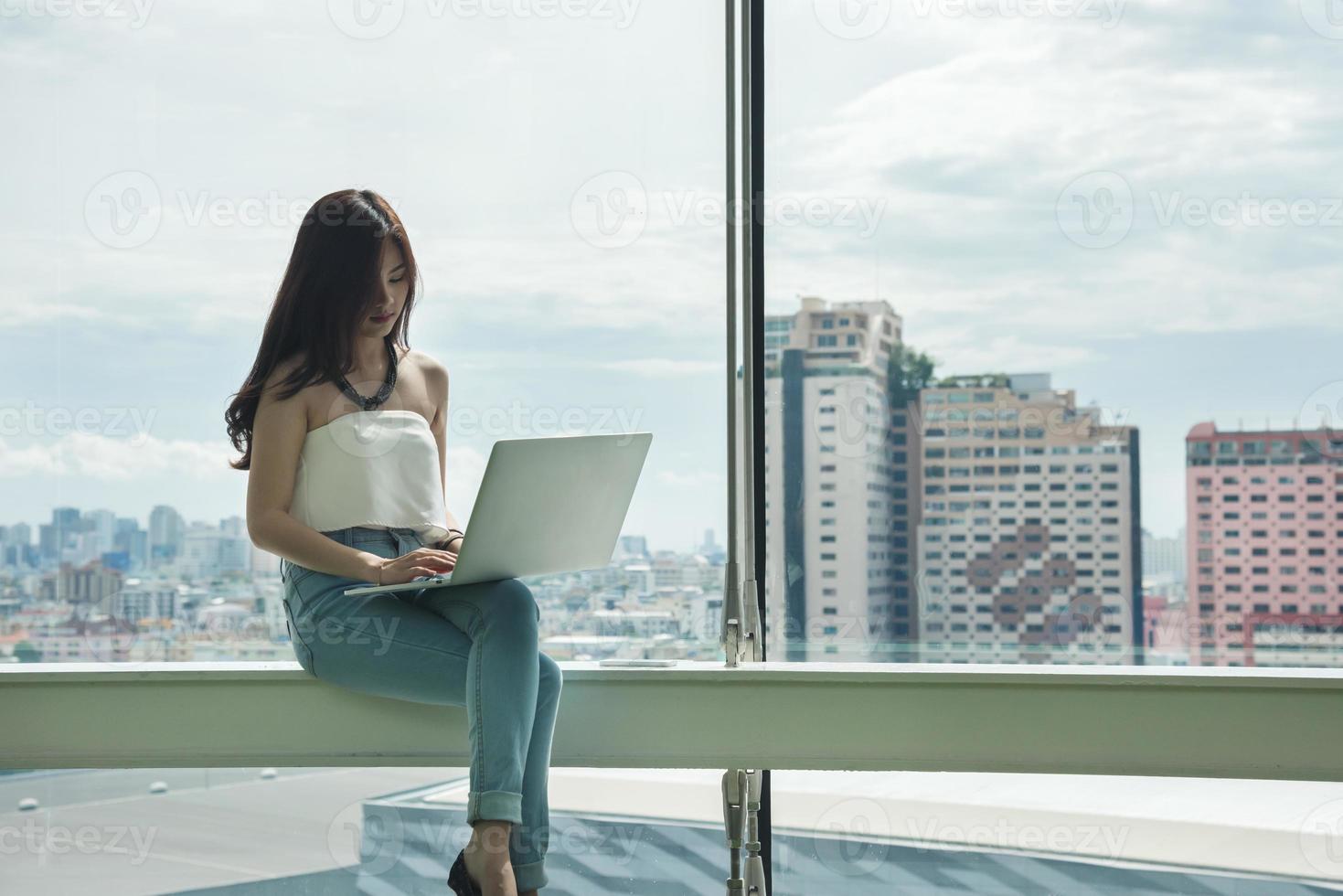 donna che utilizza computer portatile davanti alla finestra di grande paesaggio urbano foto