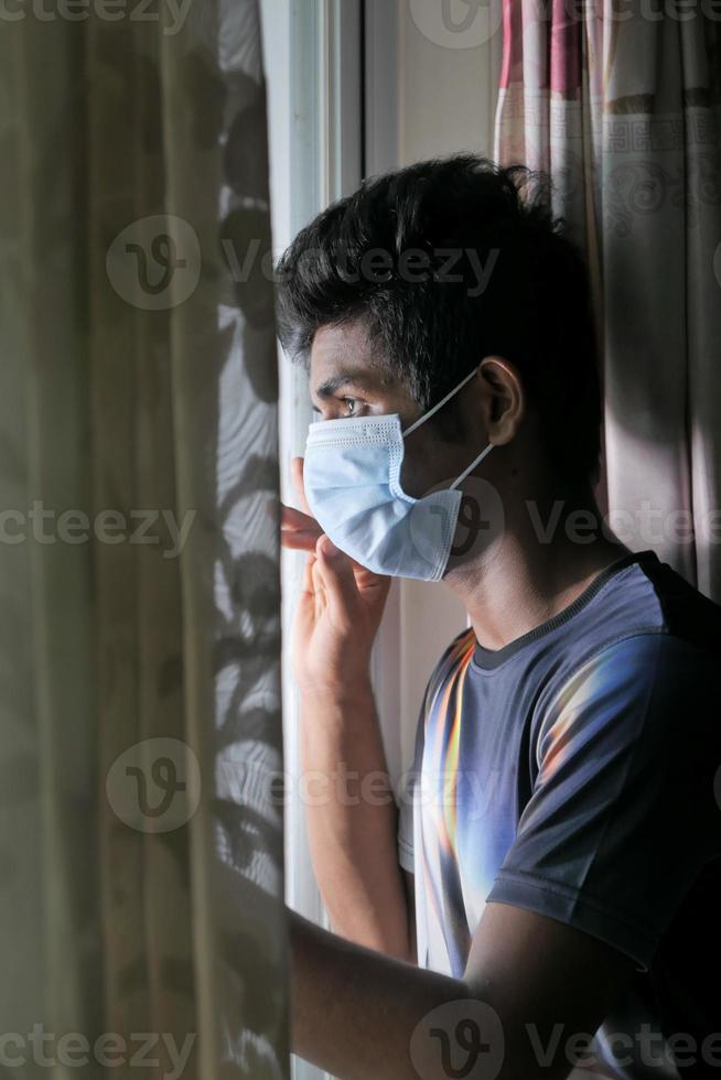 uomo che indossa una maschera guardando fuori dalla finestra foto